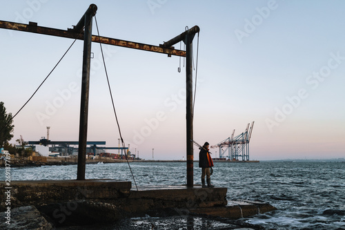 Silhouette of man fisherman wearing coat, holding rod