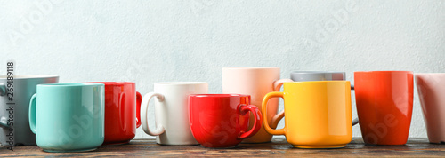 Multicolored cups on wooden table against light background, space for text photo