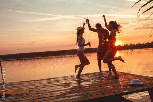 Wall Mural Group of friends dancing and having fun on the pier by the lake on sunset