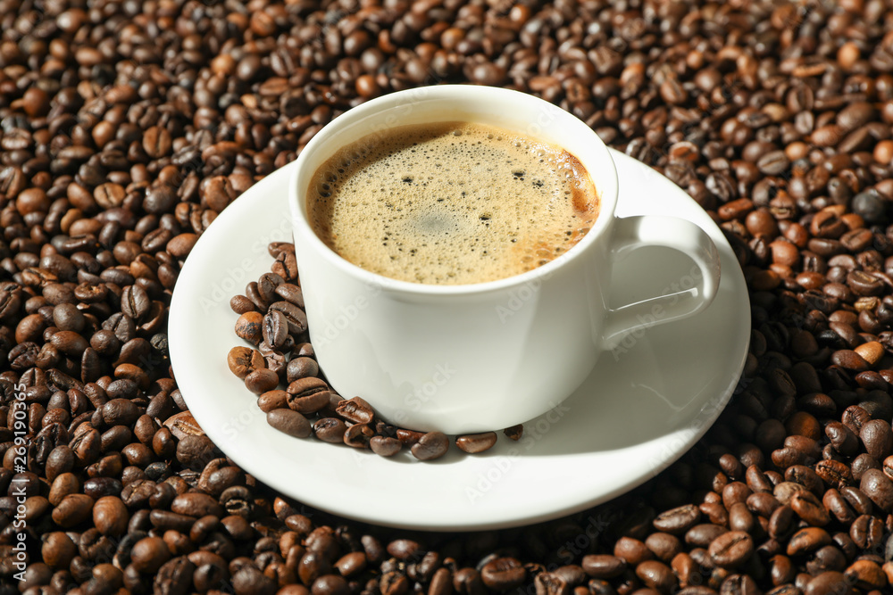 Cup of coffee with frothy foam on beans background, space for text. Coffee time accessories Cup of coffee with frothy foam on beans background, space for text. Coffee time accessories