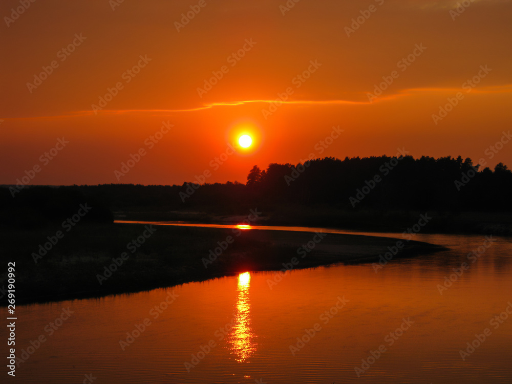 Orange solar disc in sunset under the forest river with sunlight way on the water
