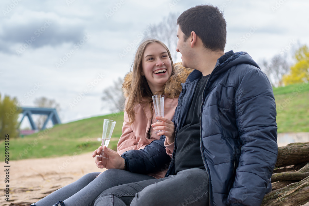 Young couple is sitting on the beach holding glasses in their hands and laughing Young couple is sitting on the beach holding glasses in their hands and laughing