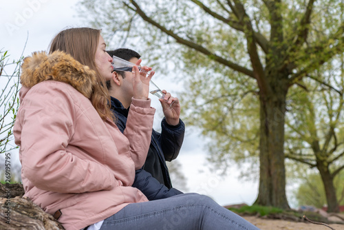 Young couple is sitting on the beach holding glasses in their hands and drinking