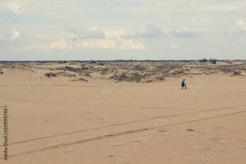 Sand dunes, dry grass, white clouds on the blue sky on the horizon, in the distance the boy walks in the sand .