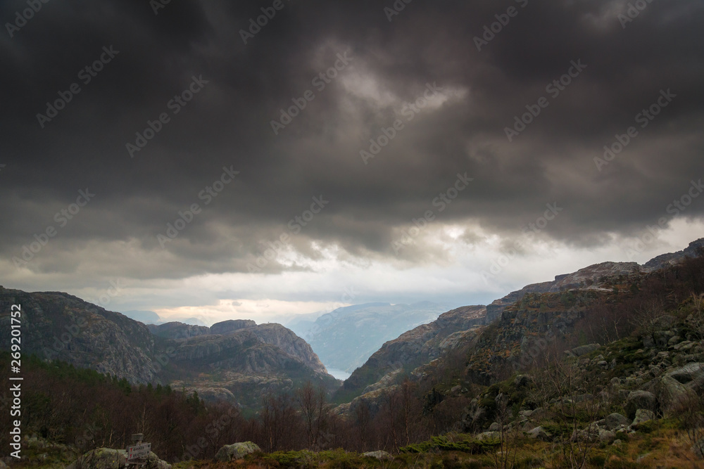 Dark stormy clouds above valley, forest and rocky mountains on background. Norway