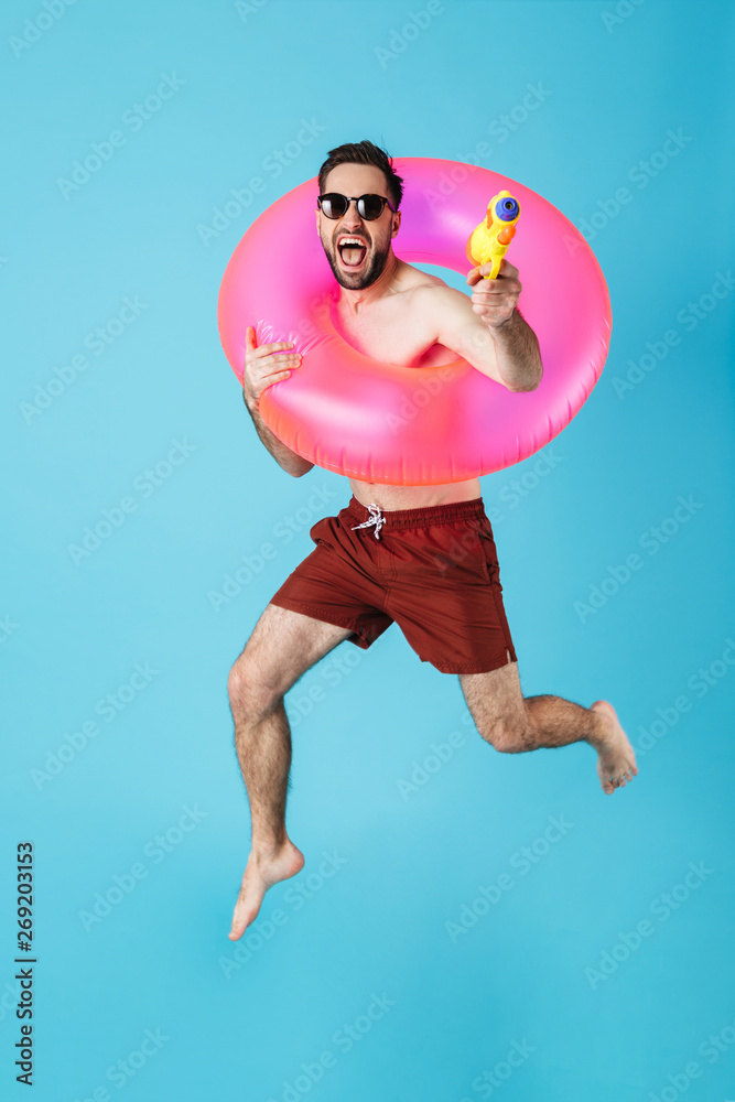 Photo of european shirtless tourist man wearing rubber ring smiling while playing with water gun toy Photo of european shirtless tourist man wearing rubber ring smiling while playing with water gun toy