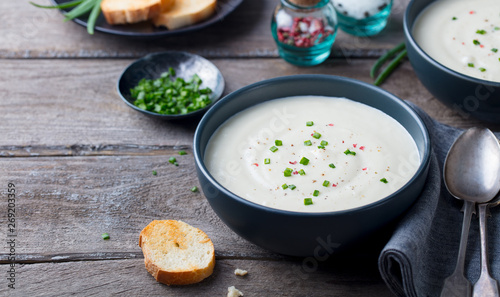 Cauliflower and potato cream soup with green onion in a bowl on grey wooden background. Copy space.