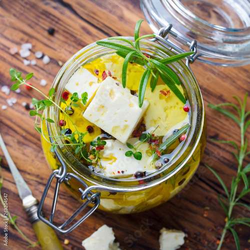 Feta cheese marinated in olive oil with fresh herbs in a glass jar. Wooden background. Top view.