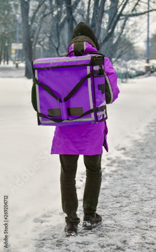 Obraz na płótnie The delivery man is walking down the street. He is wearing purple overalls and a special rectangular transport backpack. Mock up blank for text and advertising w salonie