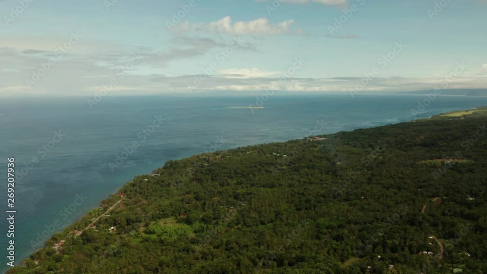 Coastline of tropical island covered with green forest against the blue sky with clouds and blue sea, aerial view. Seascape: Ocean and sky.Philippines, Camiguin. Coastline of tropical island covered with green forest against the blue sky with clouds and blue sea, aerial view. Seascape: Ocean and sky.Philippines, Camiguin.