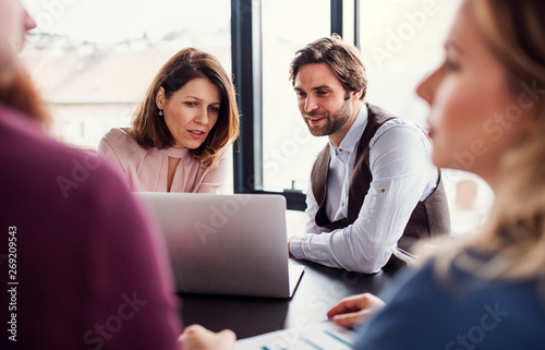 A group of young business people with laptop sitting in an office, talking.