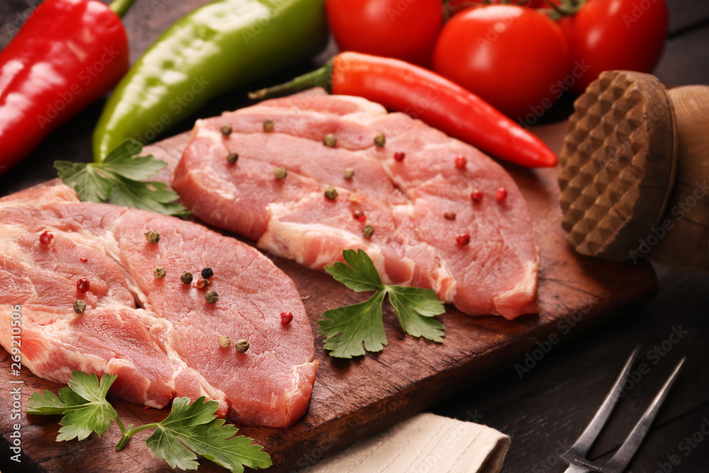 Raw meat. Raw pork steak on a cutting board with vegetables, peppers, tomato, salt and spices on a black background