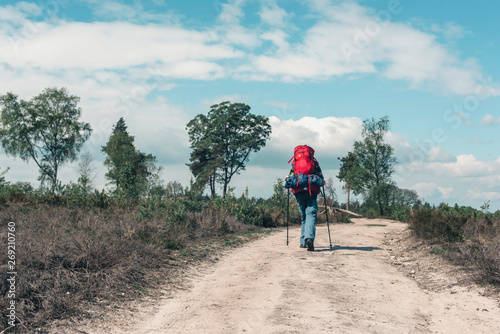 Backpacker going uphill on dirt road under blue cloudy sky.