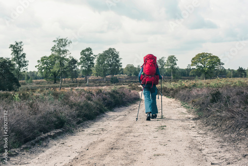 Backpacker going downhill on dirt road under cloudy sky.