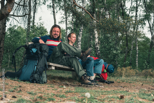Two male backpackers resting on bench in forest in spring.