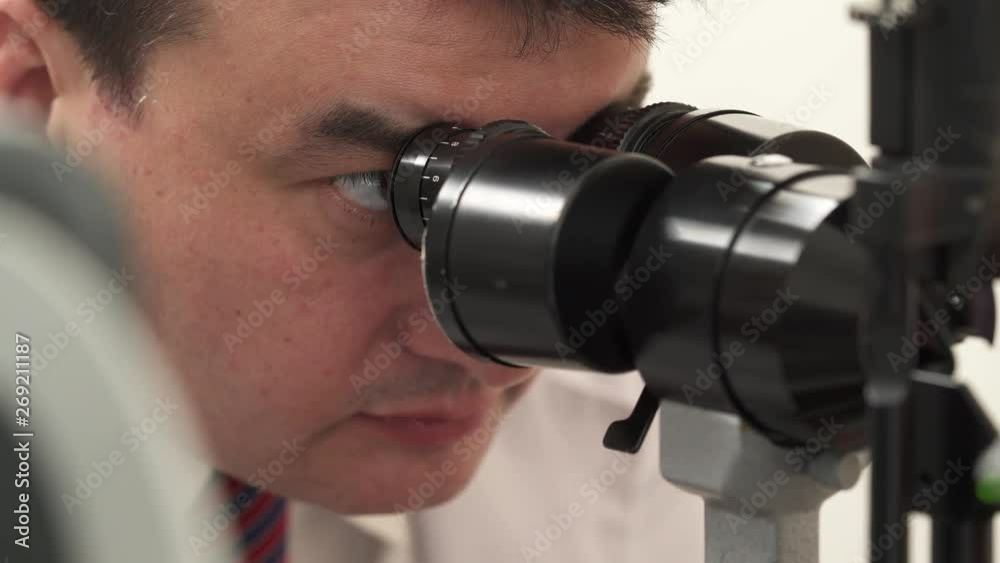 A professional doctor performing eyesight check-up using modern slit lamp. A close-up front shot of an opticians face during examination of patient A professional doctor performing eyesight check-up using modern slit lamp. A close-up front shot of an opticians face during examination of patient