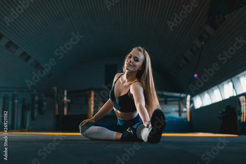 Stretching gymnast girl doing warming exercizes. View of attractive young woman doing sports at crossfit gym