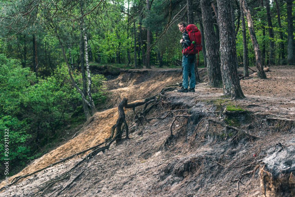 Fototapeta premium Young man with red backpack at edge of canyon in spring forest.