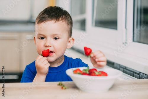 Baby boy in the kitchen eating strawberries very ripe and tasty, stocked with vitamins