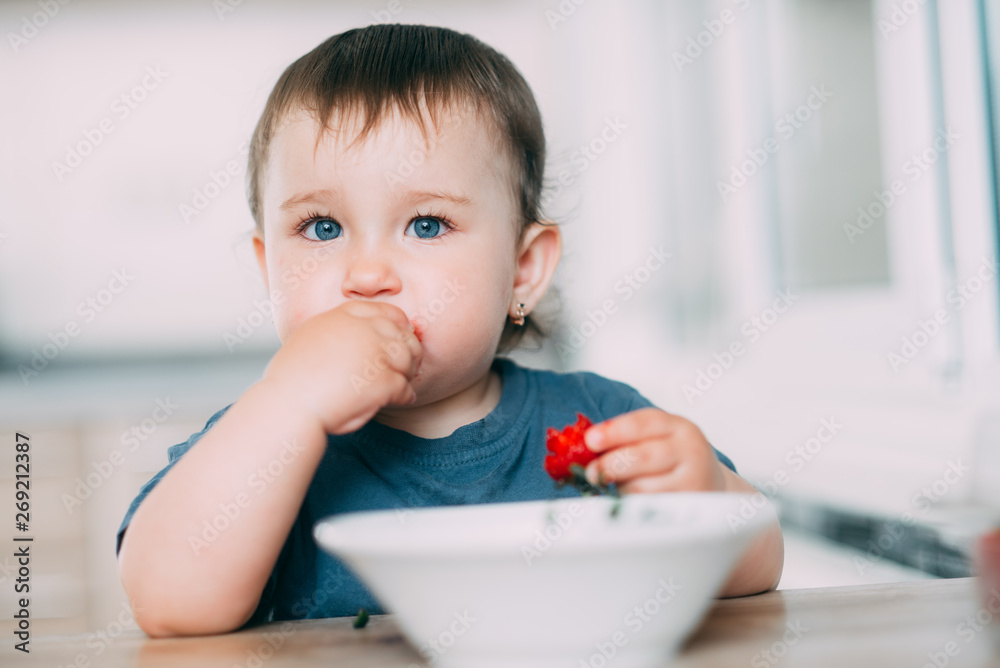A little girl in the kitchen eating ripe strawberries very appetizing and tasty A little girl in the kitchen eating ripe strawberries very appetizing and tasty