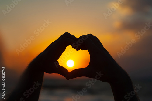 male hands in the form of heart against the sky pass sun beams. Hands in shape of love heart