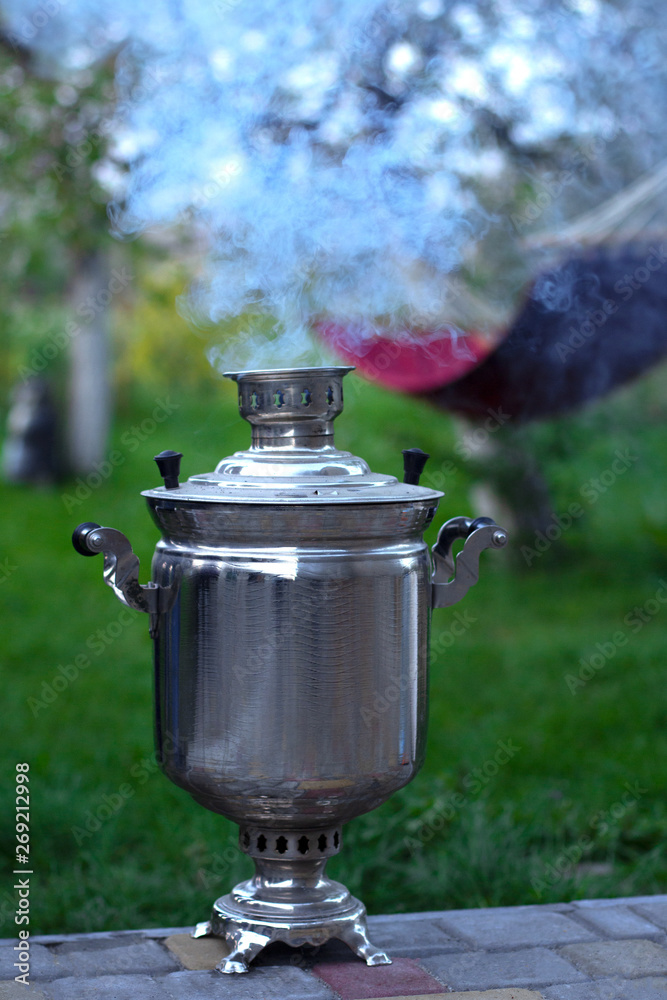 Samovar in the garden under a cherry blossom and with a hammock in the background. Homely garden. Evening in the village. Family tea Samovar in the garden under a cherry blossom and with a hammock in the background. Homely garden. Evening in the village. Family tea