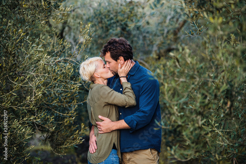 Young affectionate couple standing outdoors in olive orchard, kissing. © Halfpoint