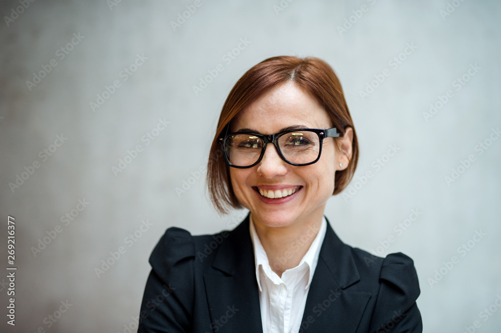 A portrait of young businesswoman standing in office, looking at camera.