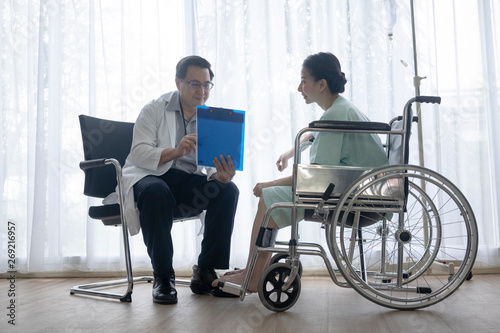 The senior male doctor talked and inquired about the patient's illness at the wheelchair of the patient.