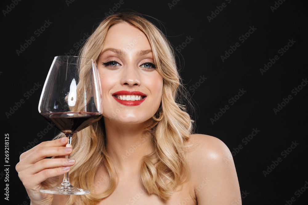 Young blonde woman with bright makeup red lips posing isolated over black wall background drinking red wine. Young blonde woman with bright makeup red lips posing isolated over black wall background drinking red wine.