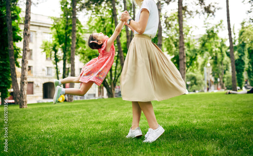 Outdoors image of happy daughter playing with her mother in the park. Loving mother and her chid spinning and enjoying the time together. Mom and little girl having fun outside. Happy Mothers day