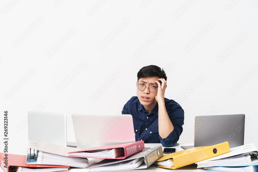 Photo of asian businessman sitting at table and using laptops while working in bright office room Photo of asian businessman sitting at table and using laptops while working in bright office room