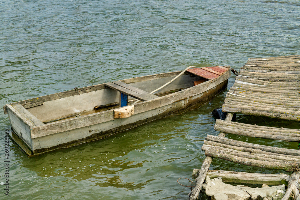 Old Wooden Rowing Fishing Boat Moored Near Lake Or River Coast In Beautiful Sunny Day Old Wooden Rowing Fishing Boat Moored Near Lake Or River Coast In Beautiful Sunny Day
