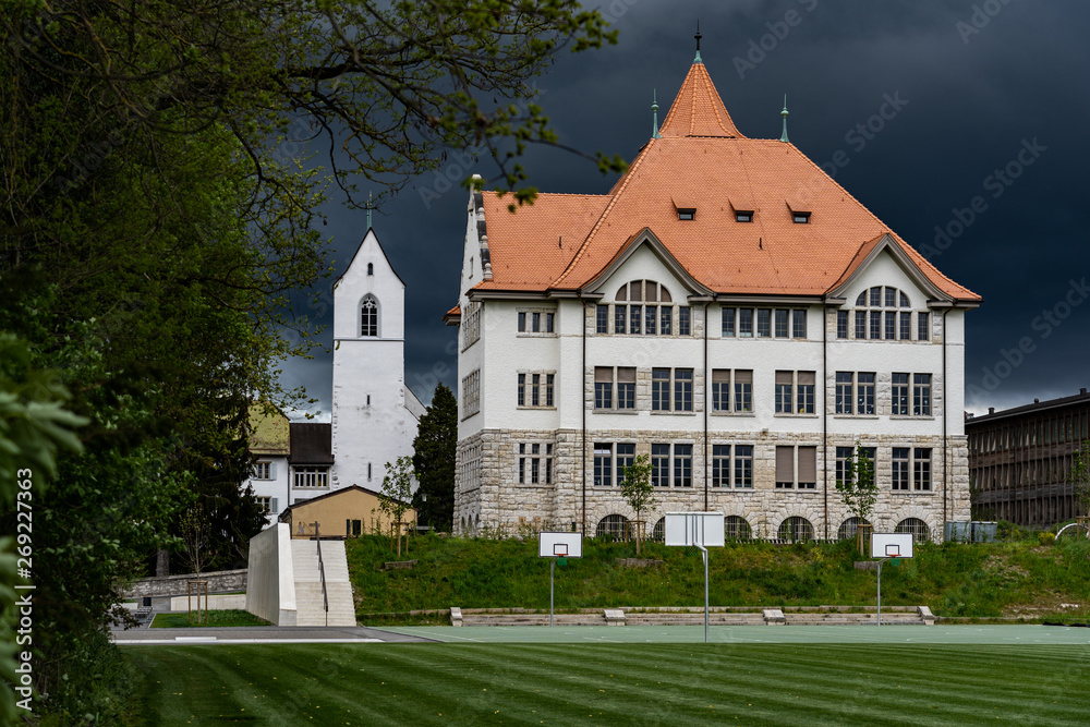 Primary school in Brugg Switzerland.  New renovated schoolhouse called Stapferschulhaus with evangelical reformed church in background. School area with soccer field in stormy weather.