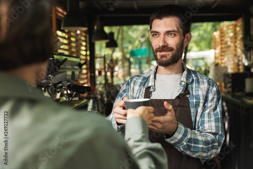 Portrait of unshaved barista man smiling while working in street cafe or coffeehouse outdoor