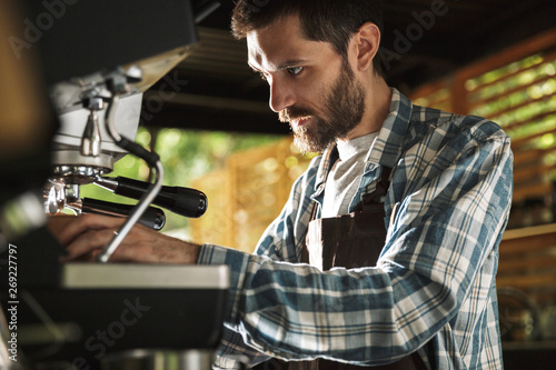 Image of happy barista man making coffee while working in cafe or coffeehouse outdoor