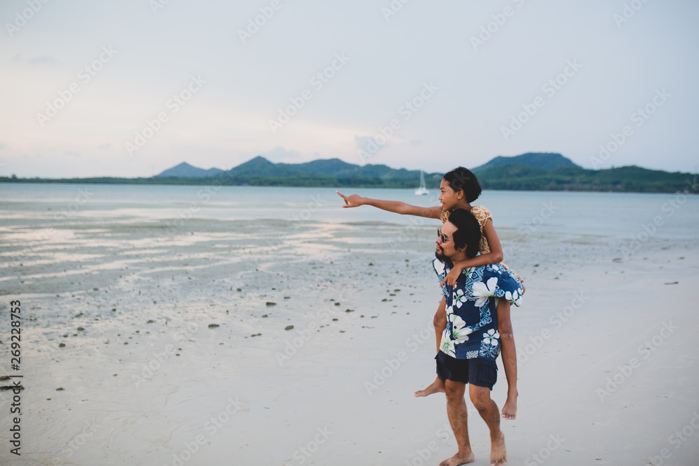 The daughter rides behind the father for a walk on the beach.