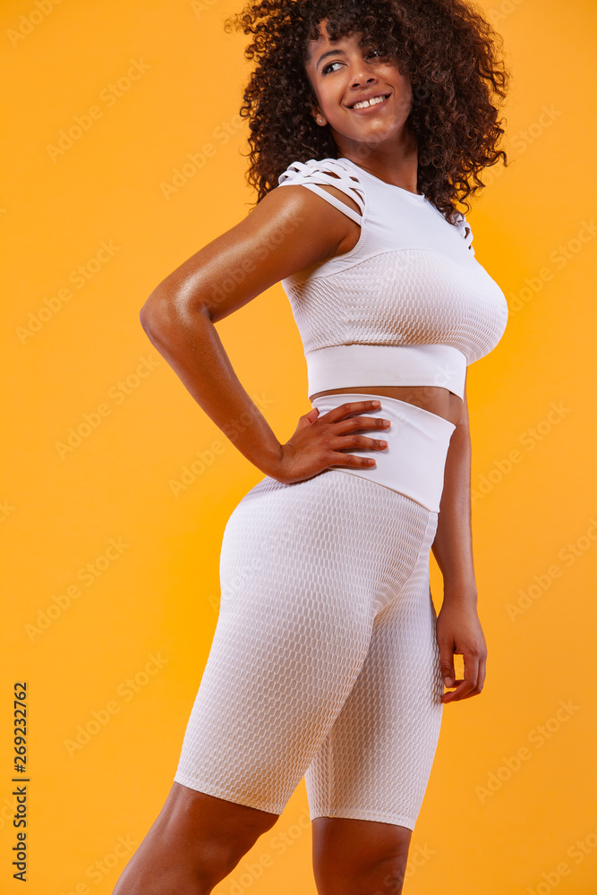 Smiling strong athletic woman with black skin and curly hair, doing  exercise on white background wearing sportswear. Fitness and sport  motivation. Stock Photo