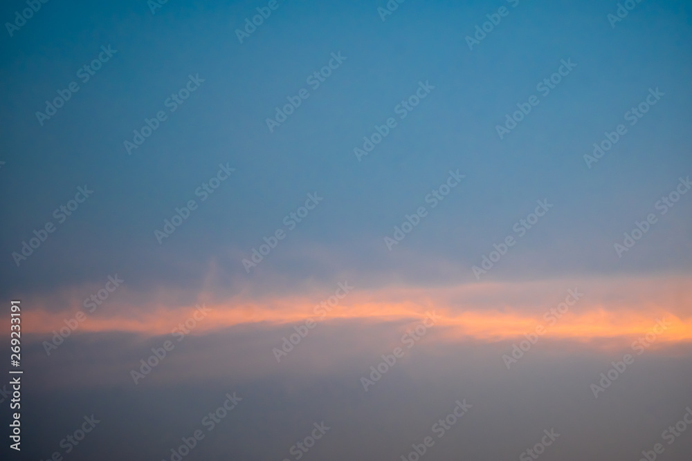 Blue sky with white fluffy clouds, orange rays of light horizontally during sunset.