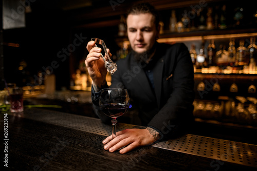 Bartender putting ice cube in alcohol cocktail