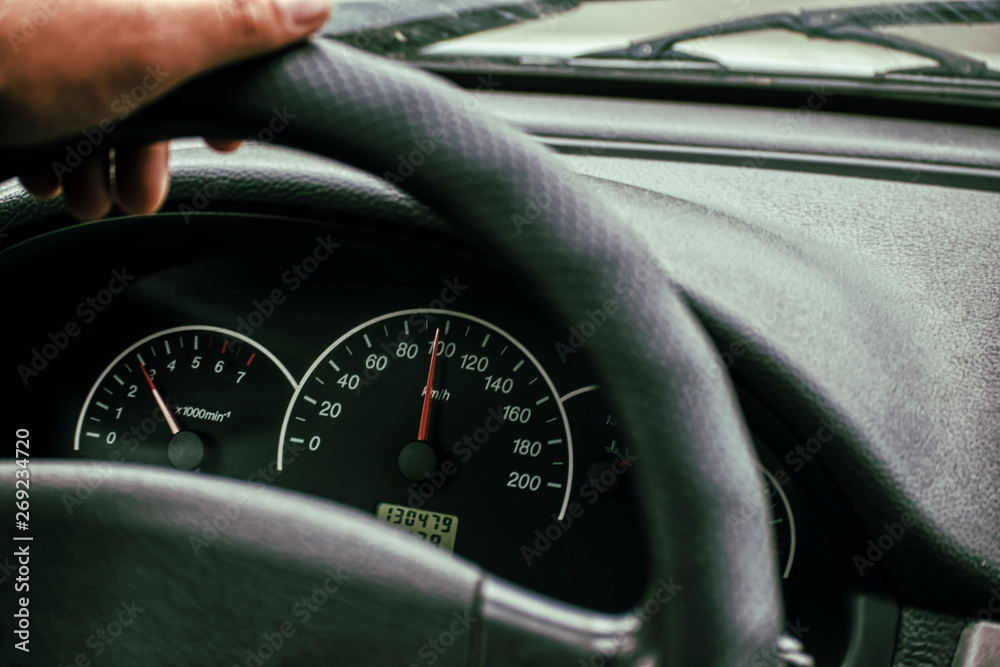 Car speedometer and driver's hand on the steering wheel.