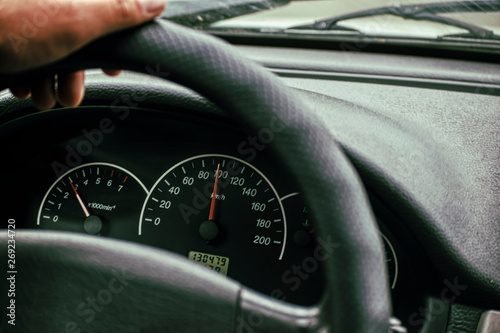 Car speedometer and driver's hand on the steering wheel.