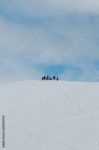 A group of snowboarders standing on the slope covered with traces and waiting for the other group members © Timofey Trushin