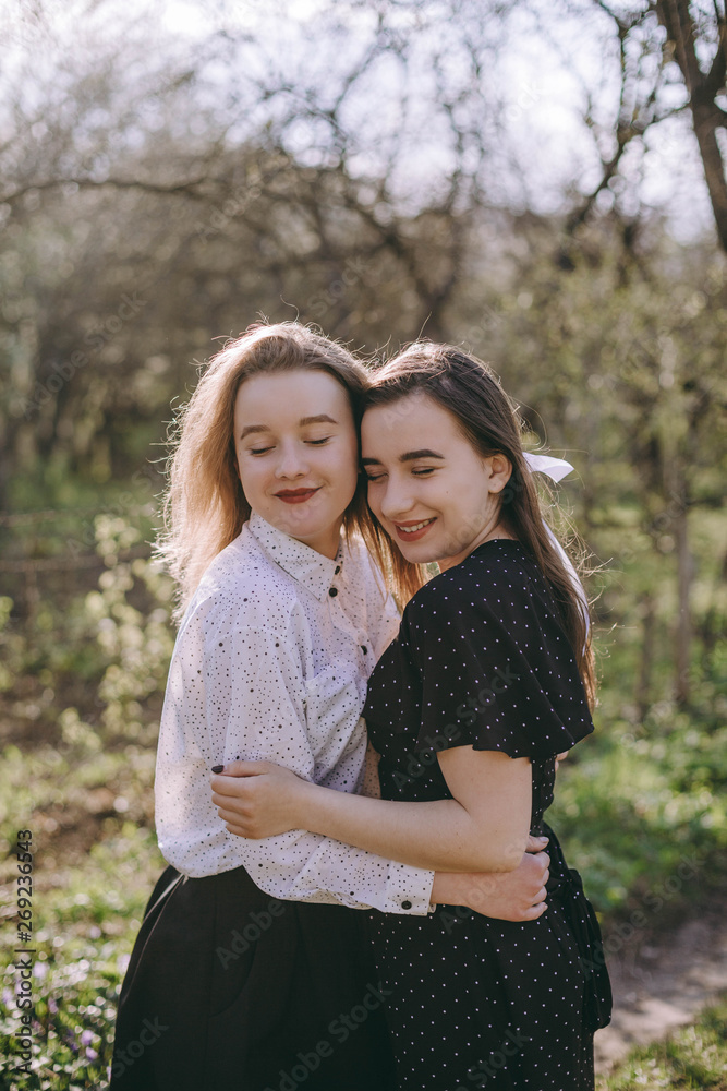 Portrait of two beautiful young sisters in the green spring garden, hugging in the field in the sunshine. Having fun together, positive emotions, bright colors. Copy space. Happy girlfriends at sunset Portrait of two beautiful young sisters in the green spring garden, hugging in the field in the sunshine. Having fun together, positive emotions, bright colors. Copy space. Happy girlfriends at sunset