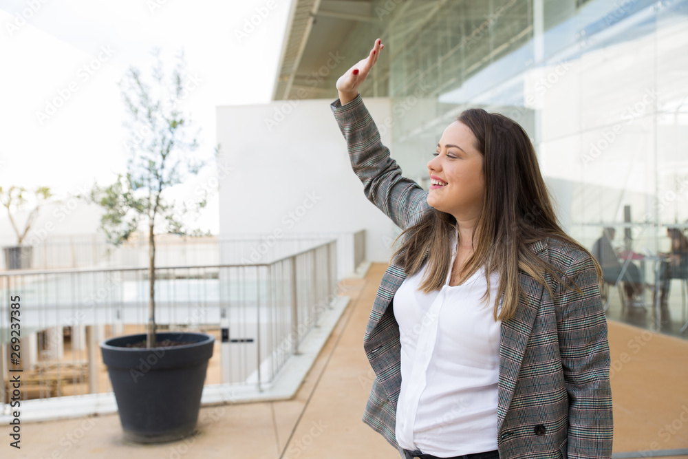 Happy business woman greeting someone outdoors. Lady looking away and standing with glass wall and railing in background. Greeting concept. Side view. Happy business woman greeting someone outdoors. Lady looking away and standing with glass wall and railing in background. Greeting concept. Side view.