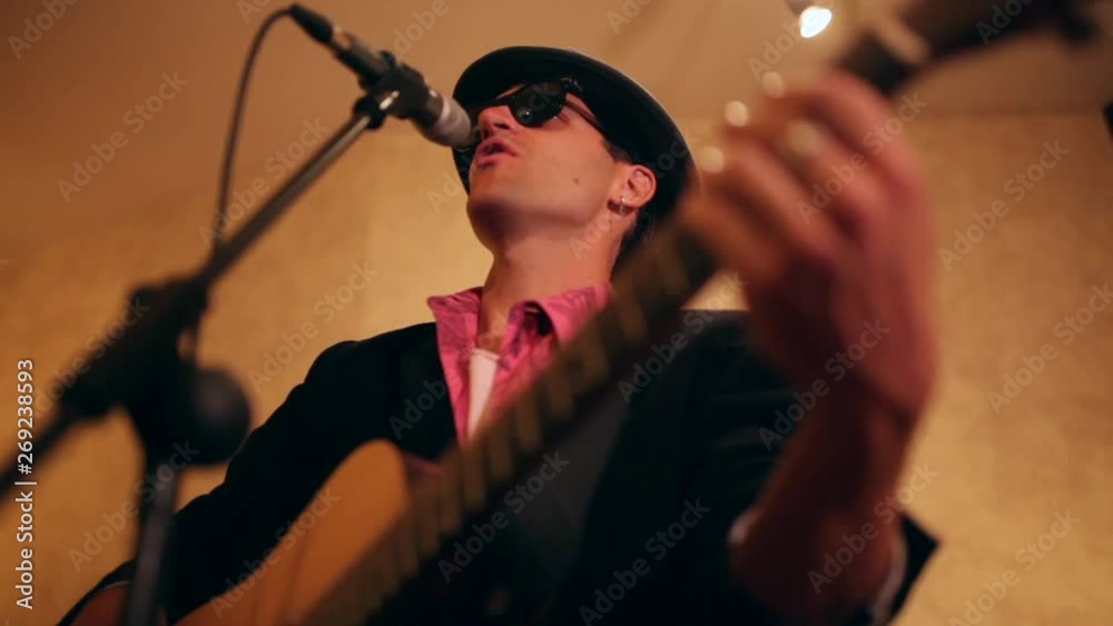 singer played the guitar in front of the microphone of a recording booth in a recording studio singer played the guitar in front of the microphone of a recording booth in a recording studio