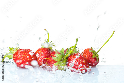 Several ripe wet red strawberries on white or colored background with splashes of water