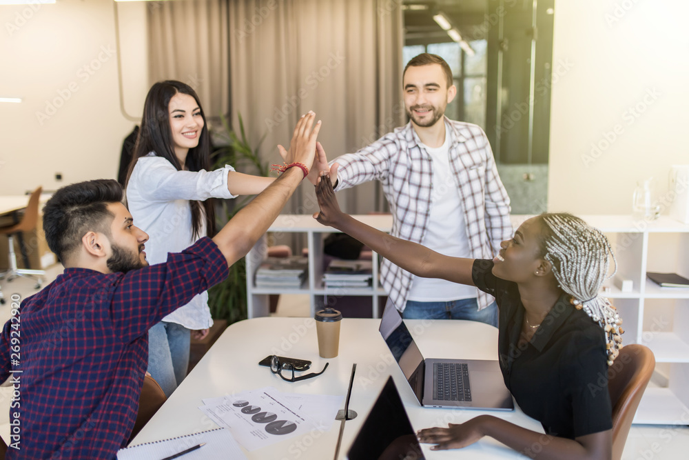 Obraz premium Group of young multiethnic diverse people gesture hand high five, laughing and smiling together in brainstorm meeting at office. Casual business with startup teamwork community celebration concept.