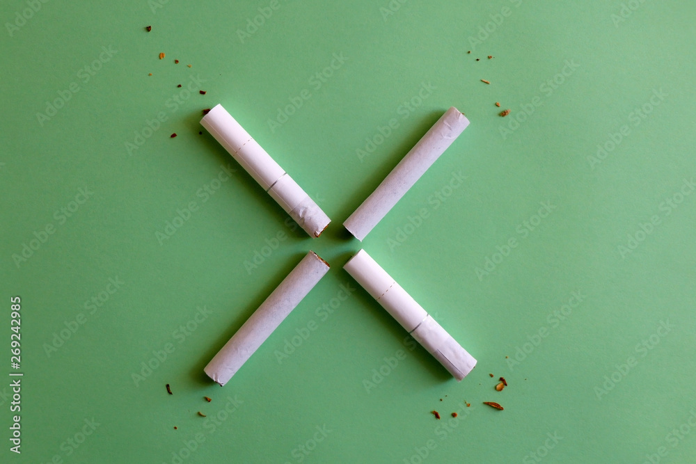 Two broken cigarettes symbolizing stop (X) sign. Smoking cessation concept. Green background. Two broken cigarettes symbolizing stop (X) sign. Smoking cessation concept. Green background.