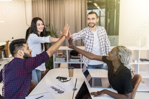 Group of young multiethnic diverse people gesture hand high five, laughing and smiling together in brainstorm meeting at office. Casual business with startup teamwork community celebration concept.